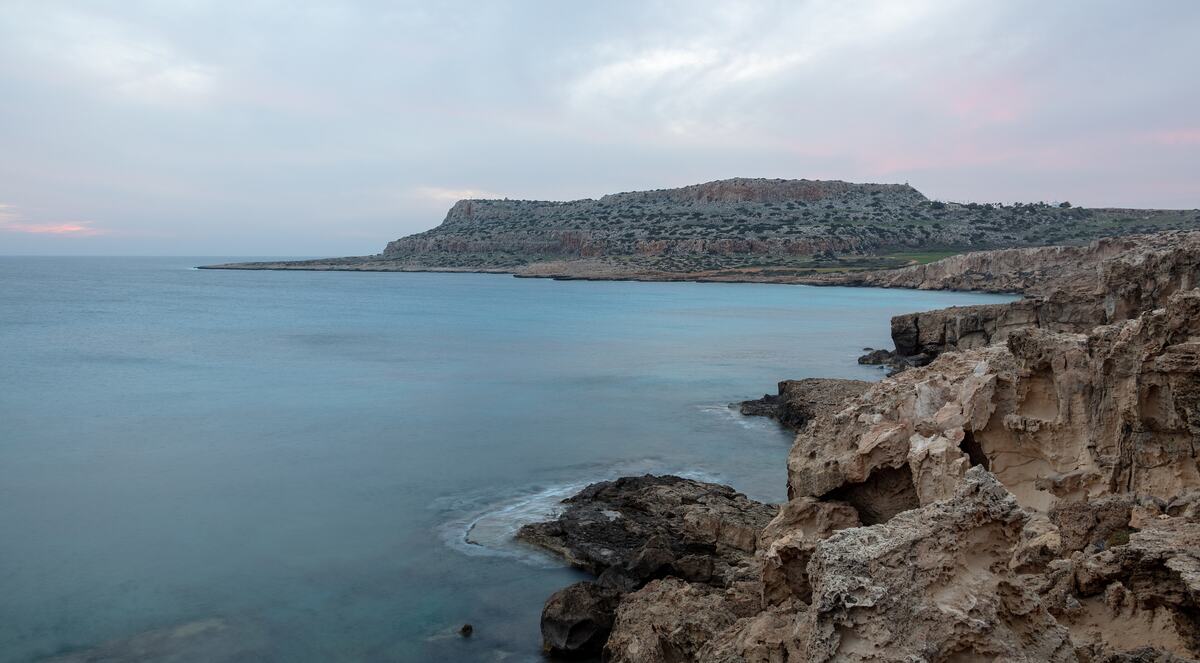 Calm turquoise water and limestone rocks at Cape Greco, with the headland stretching out to sea